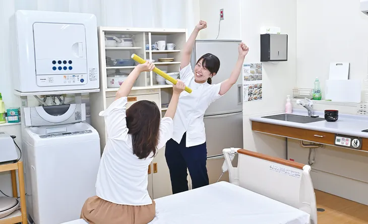 家の中を想定した設備で、棒を使った運動を一緒に行っているようす